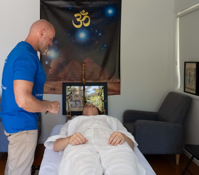 Steve standing beside a client as she lies on the treatment table, coming back into the room at the end of a session.